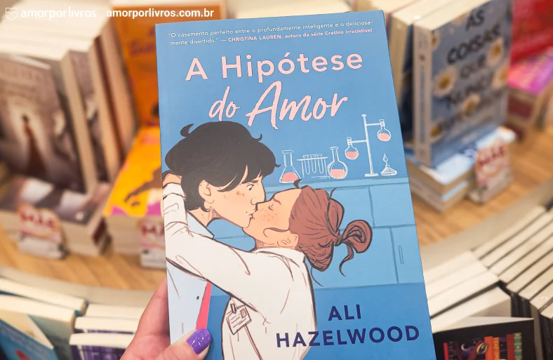 Eu segurando o livro A Hipótese do Amor com fundo de uma livraria