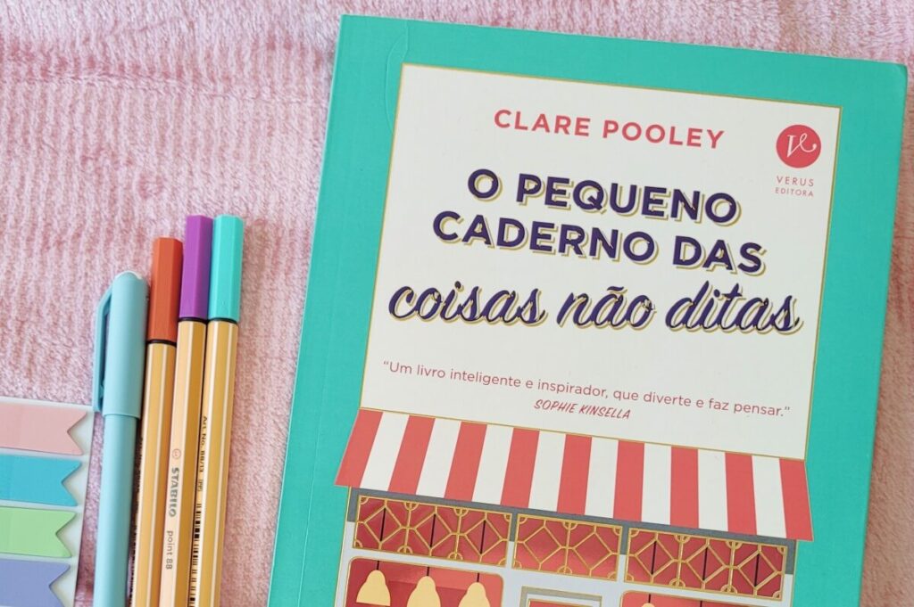 Edição física de O pequeno caderno das coisas não ditas ao lado de canetas e marcadores de página