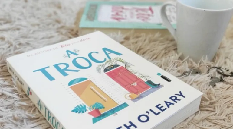 Livro A Troca em cima de um tapete peludo, com uma xícara de café
