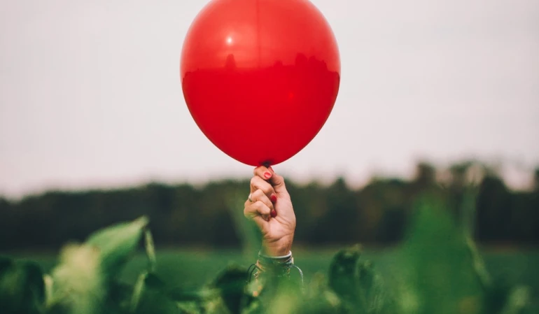 Mão segurando balão vermelho