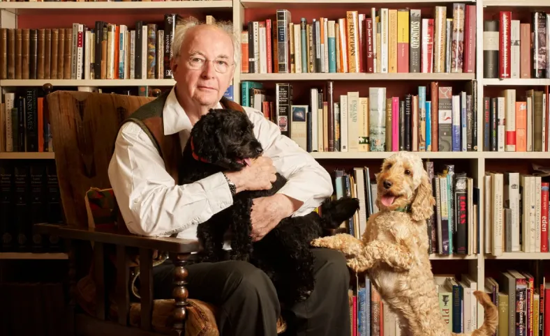 Philip Pullman sentado em uma cadeira com dois cachorros