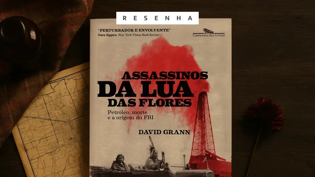 Opinião: Assassinos da Lua das Flores, de David Grann Livro Assassinos da Lua das Flores em cima de uma mesa de madeira, mapa e tecido xadrez